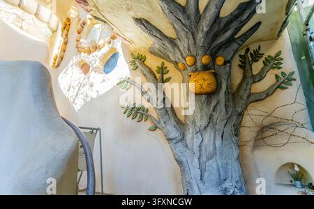 Tokio, Japan, 22. NOV 2024 - Eine strukturierte Wand zeigt einen gestalteten Baum mit einem gelben Katzen-Gesicht-Relief und grünen Blättern, beleuchtet von hellem Sonnenlicht. Stockfoto