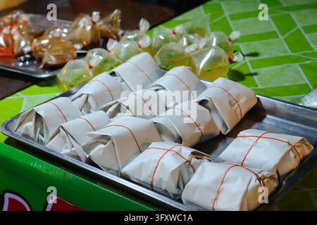 Hühnereis-To-Go-Päckchen in weißem Papier mit roten Gummibändern auf einem Edelstahltablett an einem Nachtstraßenstand in Bangkok, Thailand. Stockfoto