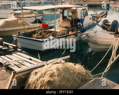 Traditionelle Fischerboote, beladen mit verhedderten Netzen, ruhen in einem ruhigen mediterranen Hafen im warmen Nachmittagslicht. Stockfoto