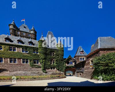 Weite Ansicht des Innenhofs der Reichsburg Cochem mit efeubedeckten Steinbauten, Rosengarten und blauem Himmel in Deutschland. Stockfoto