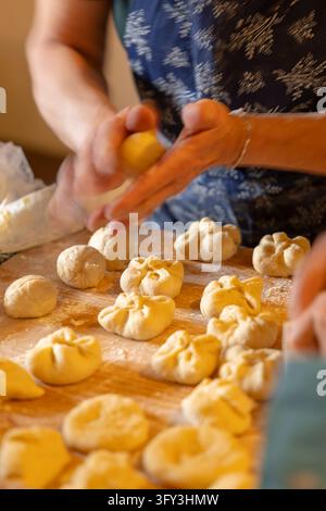 Hände formen kleine Portionen selbstgemachten Teigs zu Gebäck auf einer bemehlten Holzplatte Stockfoto