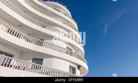 Modernes weißes Wohngebäude mit geschwungenen Balkonen vor blauem Himmel Stockfoto