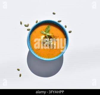 Schüssel mit cremiger orangefarbener Suppe, wahrscheinlich Kürbissuppe oder Karotten-Kürbissuppe, garniert mit frischen Kräutern und Kürbissamen, isoliert auf weißem Hintergrund Stockfoto