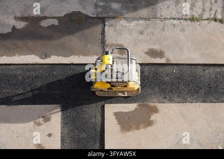 Luftbild eines Vibrationsplattenverdichters, der auf einem frischen Asphalttrog während Straßenbauarbeiten steht Stockfoto