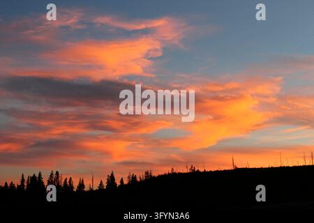 Ein dramatischer Sonnenuntergang über der Swan Lake Flat im Yellowstone-Nationalpark, Wyoming, USA. Goldenes Licht und lebendige Farben der untergehenden Sonne erhellen das weitläufige Plateau und werfen lange Schatten über die Sumpfwiesen und das Buschland, während ferne Berggipfel sich vor einem sanft glühenden, wolkenverzogenen Himmel abzeichnen. Die ruhige Wildnislandschaft unterstreicht die natürliche Pracht des amerikanischen Westens. Eine optimierte Version eines Bildes des US National Park Service. Credit: NPS / J Peaco Stockfoto