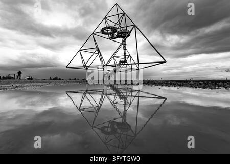 Grafische Schwarz-Weiß-Ansicht einer öffentlich zugänglichen stahlernen Tetraeder-Struktur, die sich im Regenwasser auf einer ehemaligen Bergbau-Landschaft unter d spiegelt Stockfoto