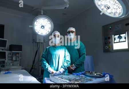 Verschiedene medizinische Kollegen in türkisfarbenen OP-Kitteln, die hinter einem abgedeckten Tisch im Operationssaal stehen. Chirurgie, Gesundheitswesen, Teamarbeit, steril, Krankenhaus, klinisch Stockfoto