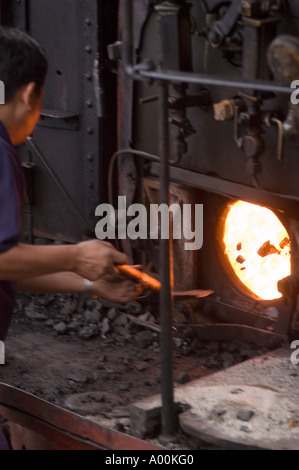 Feuerwehrmann schaufelt Kohle in die Feuerbox des berühmten Darjeeling Spielzeugzugs in Westbengalen, Indien. Stockfoto