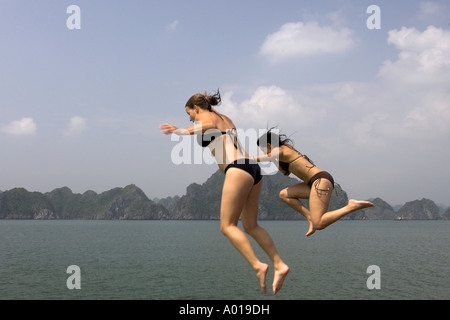 Junge Frauen springen vom Oberdeck des Kreuzfahrt-Schiff bei Monkey Island aus Cat Ba Insel Halong Bucht Vietnam ins Wasser. Stockfoto