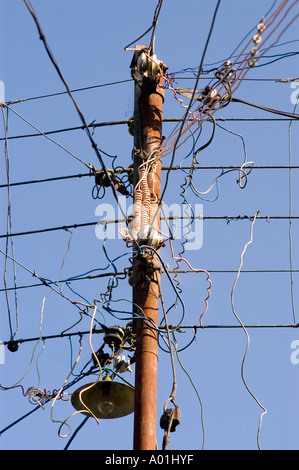 Chaotisches Elektrodrahtchaos in Indien mit verworrenen Stromleitungen und Kabeln an einem alten Versorgungsmast unter klarem blauen Himmel. Stockfoto