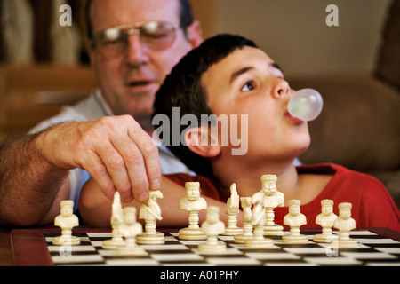 Kind 10 Jahre alt Seifenblasen aus Langeweile beim spielen Schach mit seinem Großvater Modelle veröffentlicht Stockfoto