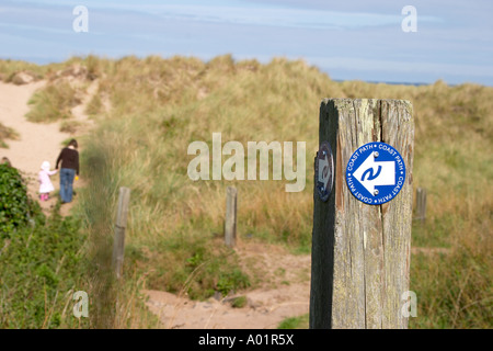Küstenpfad anmelden Holzpfosten inmitten der Sanddüne mit Mutter und Tochter zu Fuß durch die Sanddünen im Hintergrund Stockfoto