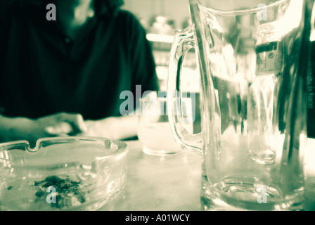 Mittelteil eines Mannes sitzend mit Aschenbecher und Gläser Stockfoto