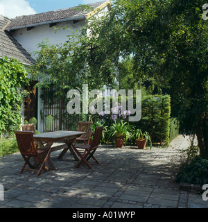 Holztisch und Stühle auf der Terrasse im Schatten von Bäumen im Garten des weißen Landhaus Stockfoto