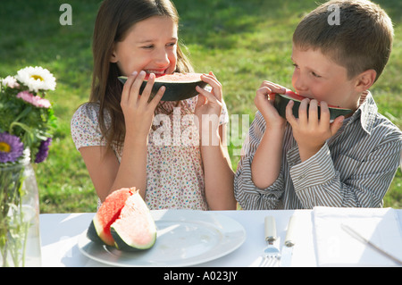 Jungen und Mädchen (7-9) am Tisch im Garten sitzen und Essen Wassermelone Stockfoto