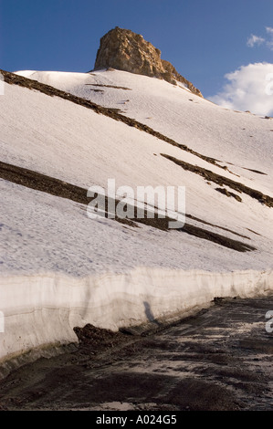 Schneebedeckte Pisten und felsiger Gipfel am Taglangla, dem zweithöchsten motorisierten Pass auf der Manali Leh Road in Ladakh, Indien. Stockfoto