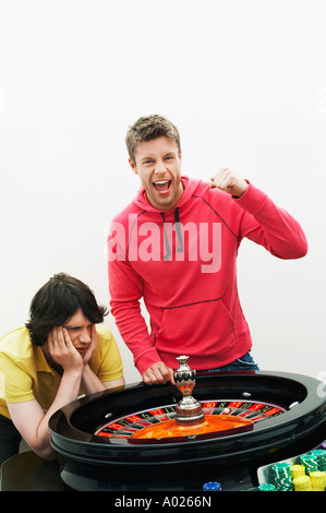 Junger Mann feiert am Roulette-Rad, während Freund verliert, Porträt Stockfoto