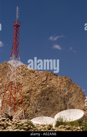 Ein rot-weißer Funkturm mit sateliten Gerichten in den Bergen des Himalaya unter einem klaren blauen Himmel. Stockfoto