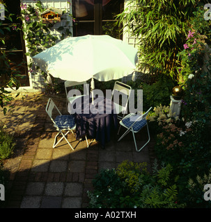 Weißen Sonnenschirm und blaue Stühle gegen Arundinaria gepflanzt in kleiner Garten im Innenhof Stockfoto