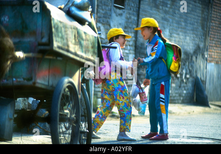 zwei junge chinesische Schulmädchen mit Schultaschen nach der Schule spielen in der Straße neben dem alten Wagen in den Seitenstraßen von der ol Stockfoto