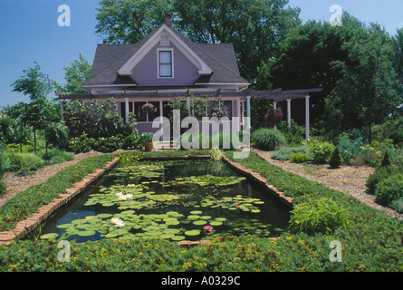 Pastellfarben Lavendel aus lackiertem Holz haus angelegten mit Ziegel und eine große dekorative Fisch und Lily Pool mit Gehweg im Garten. Stockfoto