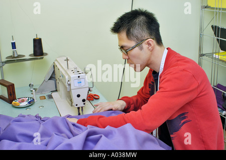 Junger asiatischer Mann, der an der Nähmaschine im Heimstudio arbeitet, Heimarbeiter, die nähen Stockfoto