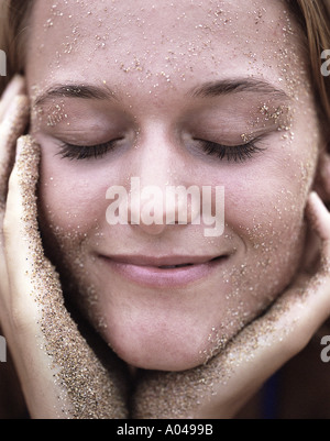 Porträt einer jungen Frau mit Sand auf ihrem Gesicht lächelnd Stockfoto