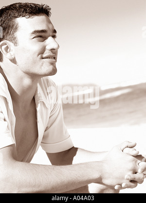 Porträt eines jungen Mannes trägt ein weißes aufgeknöpft Hemd am Strand sitzen Stockfoto