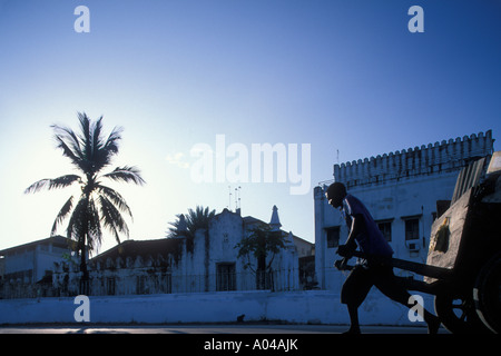 Afrika Tansania Sansibar Stone Town Mann zieht Hand gezogenen Karren in frühen Morgensonne entlang Wand außerhalb der arabischen Fort Stockfoto