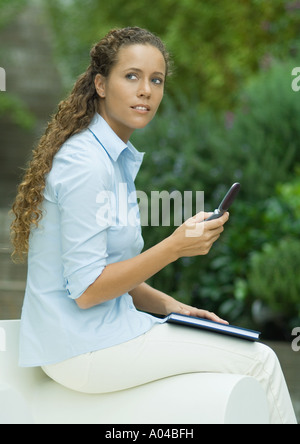 Junge Frau sitzt am Arm des Stuhls, hält Handy Stockfoto