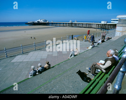 Rentner sitzen auf der Promenade mit viktorianischen Pier des 19. Jahrhunderts hinaus Blackpool, Lancashire, England, UK. Stockfoto