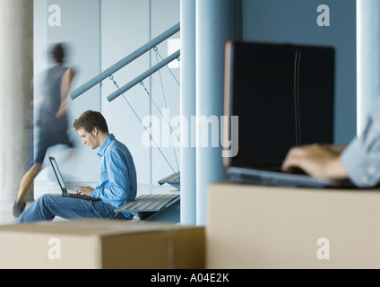 Geschäftsmann mit Laptop, zweite Person mit Laptop auf Karton in unscharfen Vordergrund Stockfoto