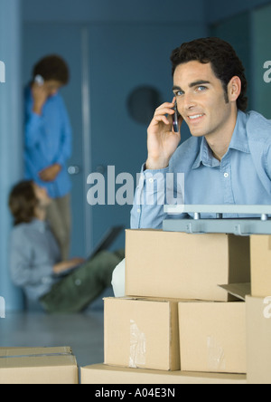 Junger Geschäftsmann mit Handy, am Tisch von Kartons unterstützt Stockfoto