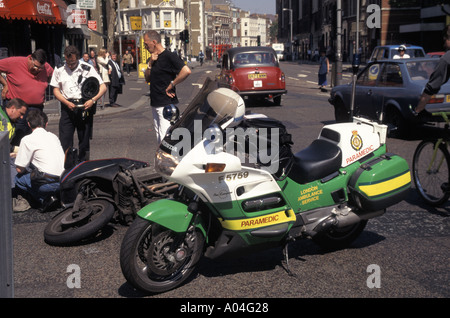 Sanitäter aus London Ambulance Service Polizei Umstehenden unterstützen Kurier Motorradfahrer nach Beteiligung bei Verkehrsunfall Stockfoto