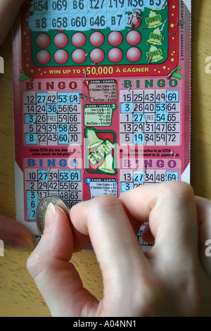 Kratzen Sie ein BINGO-Spiel mit einem Loonie von einer weiblichen hand Stockfoto