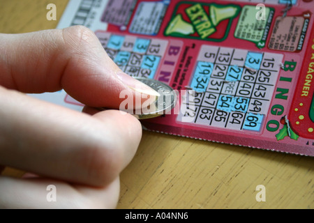 Kratzen Sie ein BINGO-Spiel mit einem Loonie von einer weiblichen hand Stockfoto