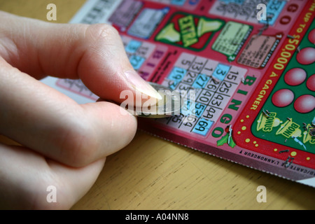 Kratzen Sie ein BINGO-Spiel mit einem Loonie von einer weiblichen hand Stockfoto