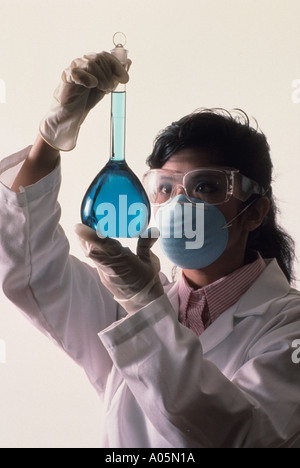 Wissenschaftlerin trägt ein Gesicht Maske, Schutzbrille und Latex-Handschuhe halten ein chemisch gefülltes Becherglas Stockfoto