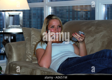 20 Jahre alte Frau zu Hause vor dem Fernseher während der Einnahme auf Telefon Stockfoto