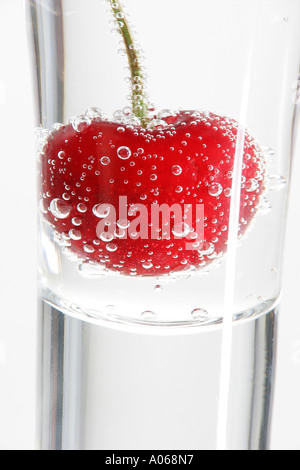 Eine Kirsche eintauchen in ein Glas Wasser Stockfoto