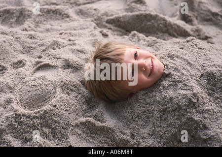 Sechs Jahre alte behaarte Blondschopf im Sand begraben Stockfoto