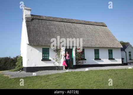 Frau und Mädchen stehen durch ein Strohdach und weiß getünchten Ferienhaus Ballyvaughan, County Clare, Irland Stockfoto