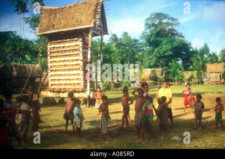 Chef der Yam Haus und Dorfkinder und Häuser im Hintergrund, Cartwheel, Trobriand-Inseln, Papua-Neu-Guinea dekoriert. Stockfoto