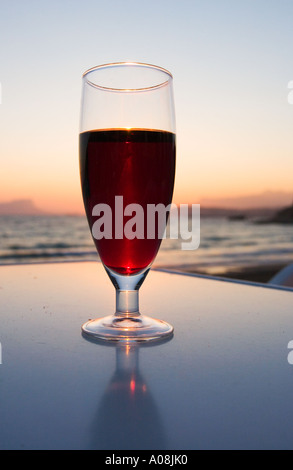 Glas Rotwein am Tisch draußen am Strand am Meer bei Sonnenuntergang Stockfoto