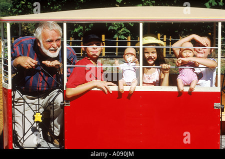 Älterer Mann mit drei Kindern in einer Spielzeugeisenbahn Stockfoto