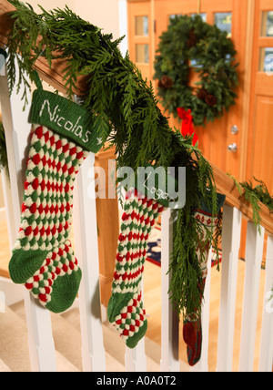 Weihnachtsstrümpfe aufgehängt auf Treppengeländer mit Tür und Kranz im Hintergrund Stockfoto