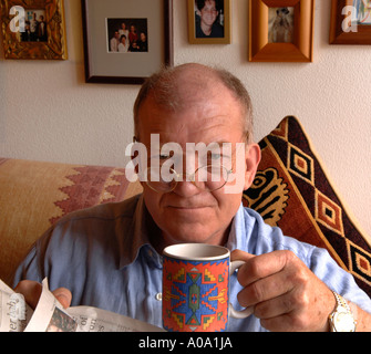 Älterer Mann mit Brille, Brille, zu Hause zu sitzen, mit Tee, Kaffee, lesen Zeitung, amüsiert Stockfoto