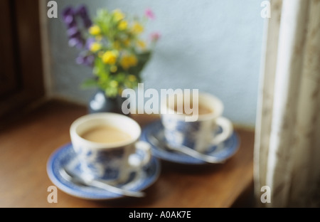 Defokussierten blaue und weiße Tassen mit Untertassen mit Tee oder Kaffee sitzen auf einer Fensterbank mit Blumen Stockfoto