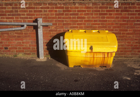 Lidern gelben Plastikeimer mit Streusalz oder Splitt vor Ziegel Wand und Verkehr Schranke in warmes Sonnenlicht Stockfoto