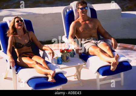 Mann und Frau tragen Swimsuites und Sonnenbaden in Liegestühlen und lachen Stockfoto